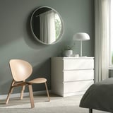 Minimalist bedroom with wood chair, white dresser, round mirror, lamp, plant, and bed. Scandinavian FRÖSET chair enhances modern atmosphere.