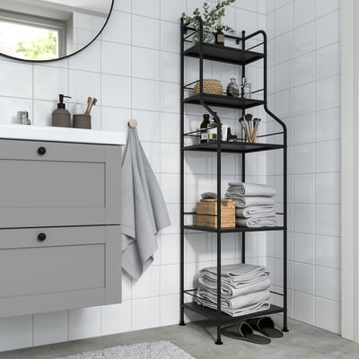 Black FRÖSJÖN shelf in bathroom with towels & toiletries, beside cabinet & mirror.