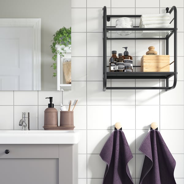 Modern bathroom with FRÖSJÖN black metal wall shelf holding towels and toiletries above sink. Two purple towels hang below.