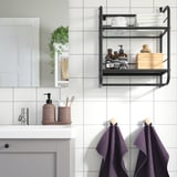 Modern bathroom with FRÖSJÖN black metal wall shelf holding towels and toiletries above sink. Two purple towels hang below.