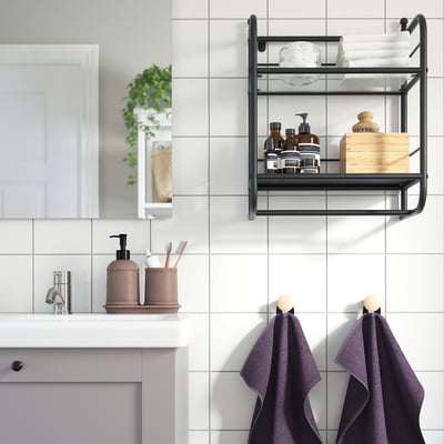 Modern bathroom with FRÖSJÖN black metal wall shelf holding towels and toiletries above sink. Two purple towels hang below.