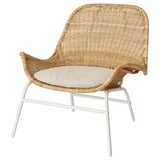 Natural-rattan armchair with beige cushion, white metal legs, woven design, curved back & arms.