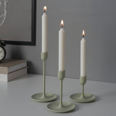 Three lit candles in green holders of varying heights on a table, creating a warm ambiance.