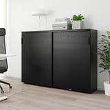 GALANT black cabinet, slim, tall, with sliding doors, in office setting with plants & chair.