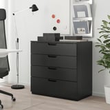 GALANT ikea chest: black 4-drawer unit beside desk, chair, lamp. Top has boxes, papers. Background: whiteboard, bookshelf.
