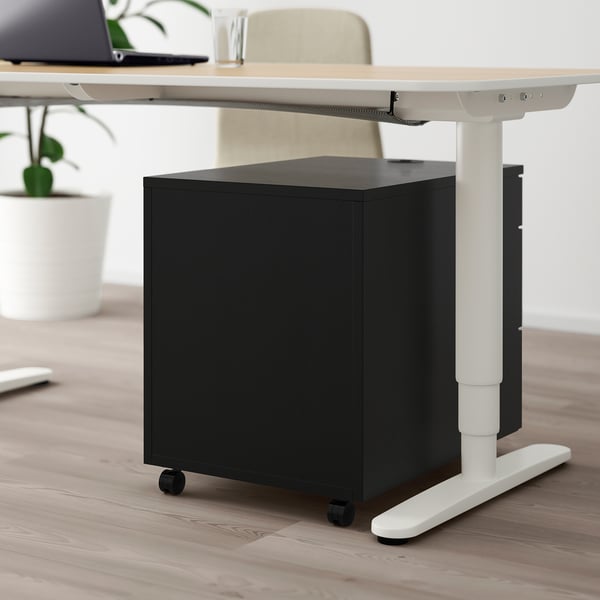 Black rolling filing cabinet under adjustable desk with lock for secure storage.