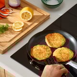 Flipping potato pancakes in black pan. Lemon, onion, herbs nearby.