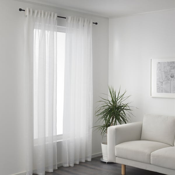 Sheer curtains by window, daylight filters in. Armchair and plant right side.