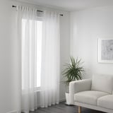 Sheer curtains by window, daylight filters in. Armchair and plant right side.