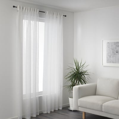 Sheer curtains by window, daylight filters in. Armchair and plant right side.