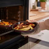 Person placing dark-grey oven dish filled with roasted vegetables into an open oven.