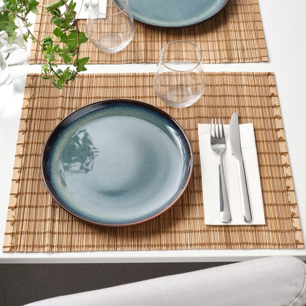 Two table settings with blue plates, glasses, cutlery, and plant on bamboo mats.