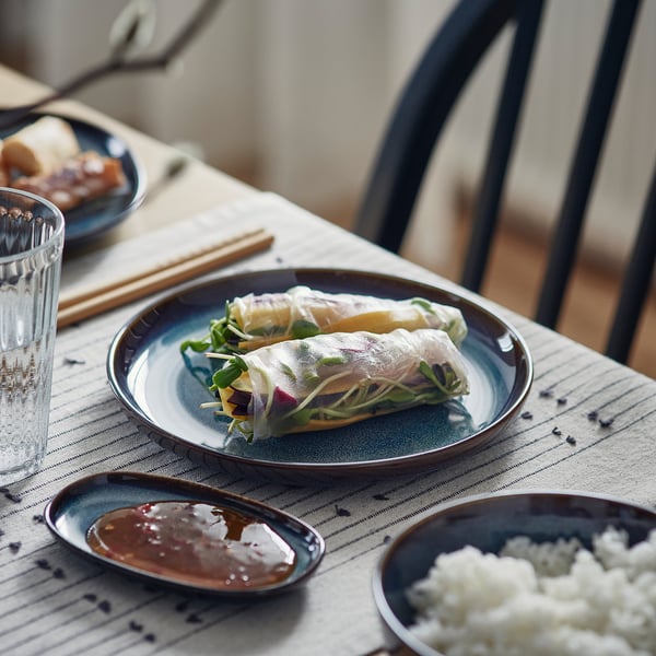 Blue glazed plate with rolled food, sauce, and rice. Served with chopsticks.
