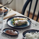 Blue glazed plate with rolled food, sauce, and rice. Served with chopsticks.