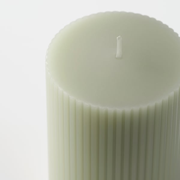 Close-up of stylish, ribbed green candle with cotton wick, set against bright background.