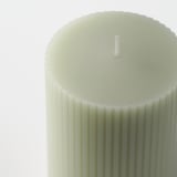 Close-up of stylish, ribbed green candle with cotton wick, set against bright background.