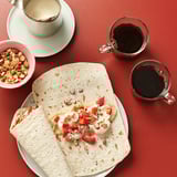 Image a red table with GRÄDDAT flatbreads, berries, cream, nuts, and soft drinks.