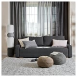 Modern gray sofa-bed with colorful pillows, round poufs, and tall white lamp.