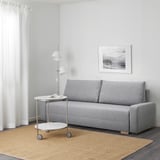 Modern living room with gray sofa-bed, side table, floor lamp, and framed photo.