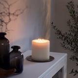 White candle on a table beside dark vases, casting warm light.