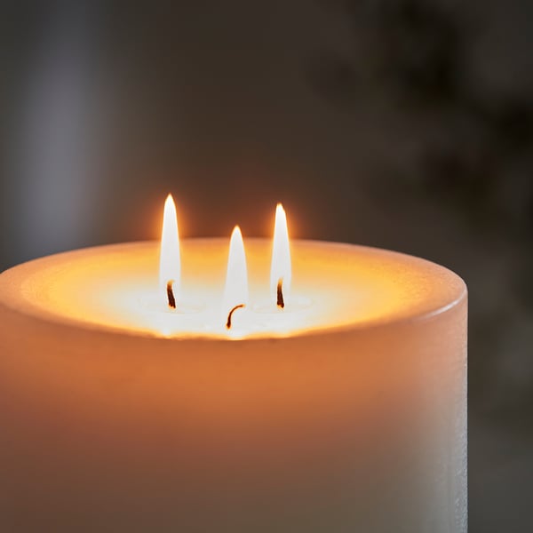 Three lit wicks on an orange candle, emitting a warm, inviting glow, well-crafted with quality materials.
