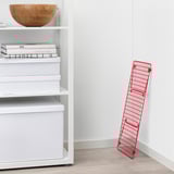 Red metal shoe rack leans against a wall next to a shelf with books and boxes.