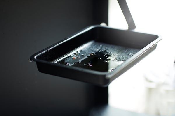 Black rectangular tray with water droplets, handle on right, on dark surface.
