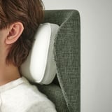 Person using white headphones, leaning on green cloth-covered headrest.