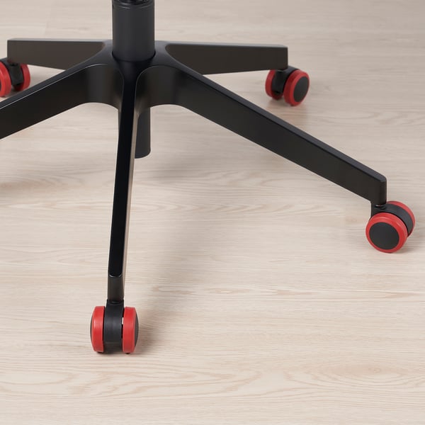 Image description: close-up of a black swivel chair base with red casters on a light wooden floor.