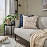 Cozy living room: grey sofa with GULDFLY off-white pillow, plant, laptop table, curtains.