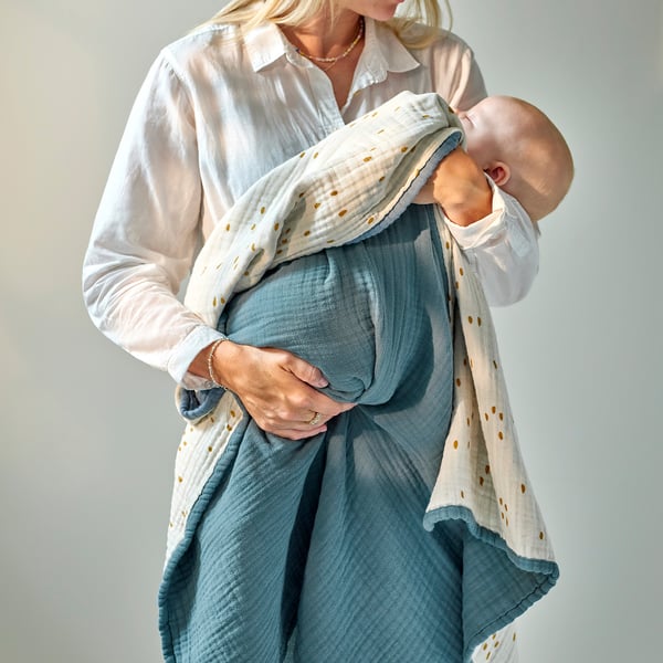 A woman holding a sleeping baby wrapped in a soft, thick, blue and white dot blanket.