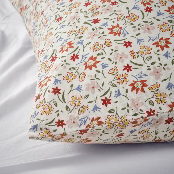 Floral patterned cushion on a white bed. Bright colors, recycled cotton.