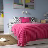 Bright pink GULLSTRÅLE bedspread in soft fleece covers large bed, with patterned pillows, cosy decor.