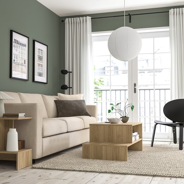 Modern living room with GULLSUDARE lamp over coffee table, warm glow, large windows, beige sofa, black chair.