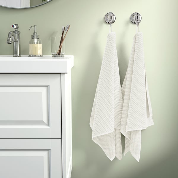 Neat white towels hang by chrome hooks beside a white sink vanity with green walls.