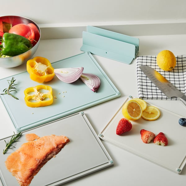 Three light blue cutting boards with different ingredients: sliced bell pepper, red onion, lemon, strawberries, salmon, and knife, stored neatly.