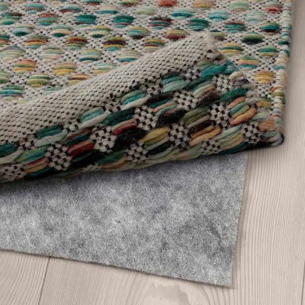 Multicolored woven rug on a wooden floor with a gray non-slip mat underneath ensuring stability.