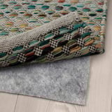Multicolored woven rug on a wooden floor with a gray non-slip mat underneath ensuring stability.