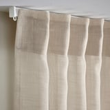 Sheer beige curtains hang with pleated folds, offering privacy while allowing daylight in.