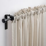 Light beige curtains hang with pleats using modern black rod and finials.