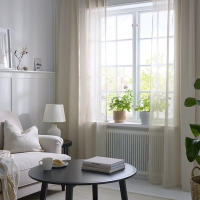 Bright living room with light beige HÄLLEBRÄCKA sheer curtains, modern furniture, and a cozy armchair.