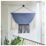 Hovering macramé by sofa, blue hanging textile with fringes, wall art.