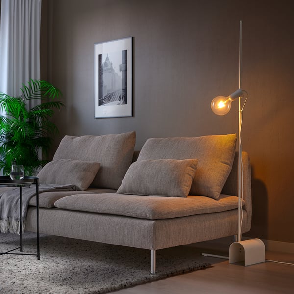 Modern room with grey HÅRSLINGA lamp beside couch. Tall, sleek design with warm light bulb.