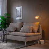 Modern room with grey HÅRSLINGA lamp beside couch. Tall, sleek design with warm light bulb.