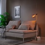 Cozy living room with HÅRSLINGA lamp next to sofa, illuminating side table with wine glass and plant against dark wall.