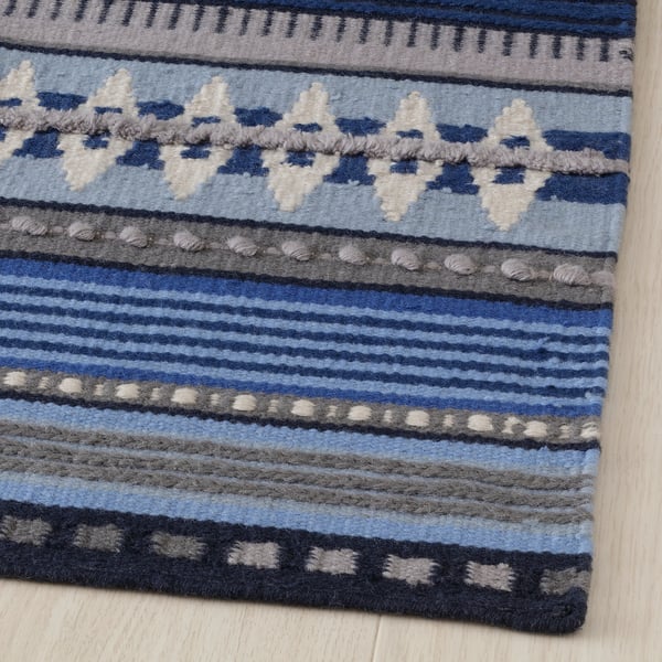 A vibrant, handwoven rug with intricate geometric patterns, showcasing a mix of smooth and textured wool in shades of blue and gray.