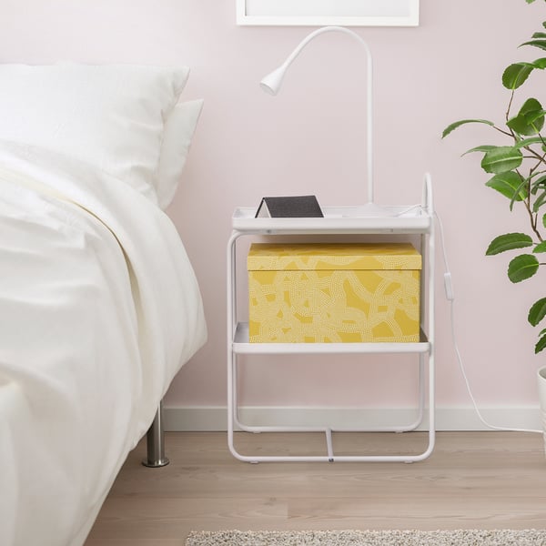 Small bedside table with shelves holds a lamp and box, ideal for space-saving next to a bed.