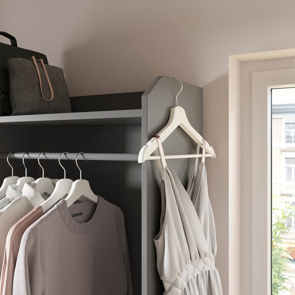 Modern closet with gray fabric drawers, white hangers, light gray dress, and white walls. A bag and black coat hang at the top.