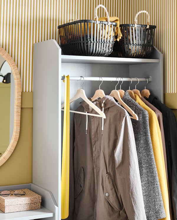 Modern closet with gray shelves, yellow handle, brown clothes, and black baskets against beige striped wall.