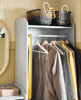 Modern closet with gray shelves, yellow handle, brown clothes, and black baskets against beige striped wall.